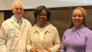 Three doctors standing together, the one in the middle is holding an award