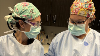 Surgeons in sterile clothing and protective equipment preparing for a procedure.