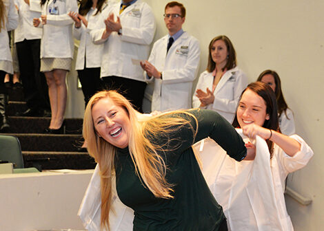 Sarah Klepp, '20, is helped into her white coat by Carly Miller, '19